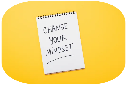 Weißer Notitzblock mit schwarzer Schrift "Change your Mindset" auf gelben Untergrund