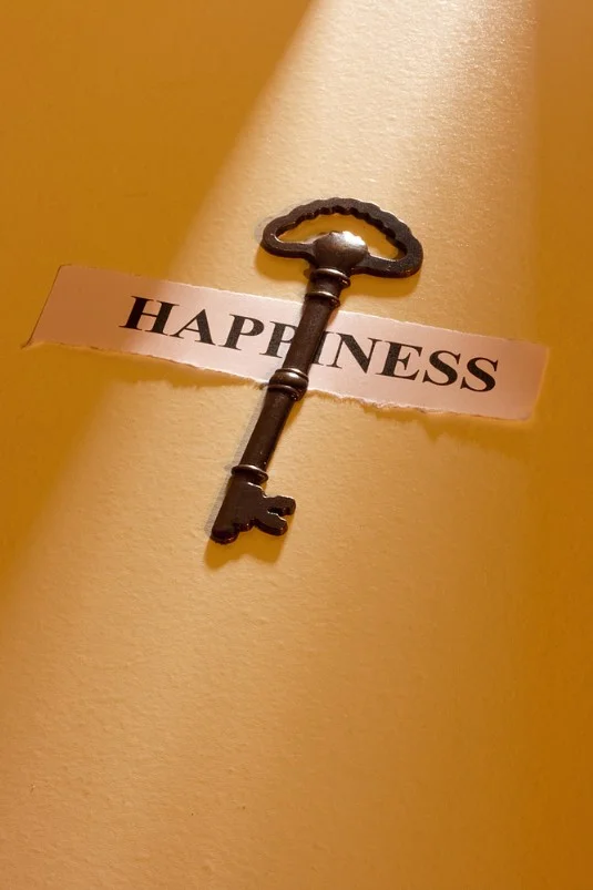 goldener Schlüssel liegt auf einem schmalen Blatt mit Aufsschrift:" Happiness", Hintergrund okkerfarben